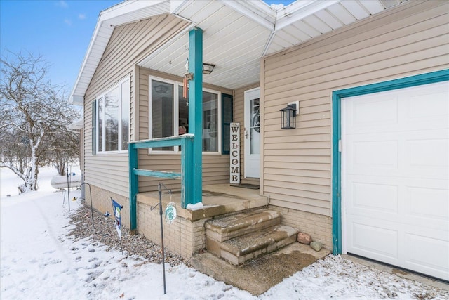 snow covered property entrance featuring a garage