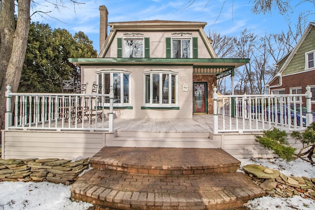 snow covered property with brick siding, a chimney, and a wooden deck