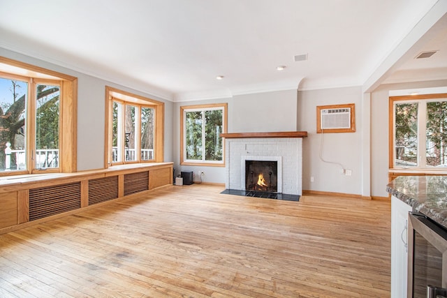 unfurnished living room with an AC wall unit, ornamental molding, a brick fireplace, and light wood-style flooring