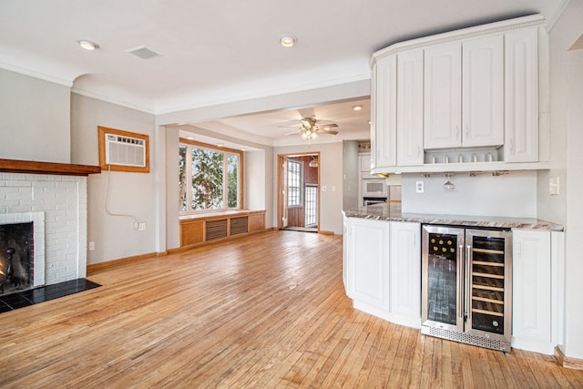 kitchen with wine cooler, light stone counters, a fireplace, white cabinets, and light wood finished floors