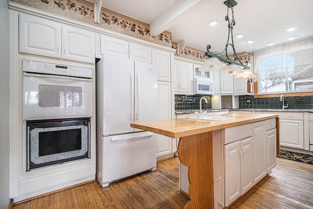 kitchen with hanging light fixtures, white appliances, a center island with sink, and white cabinets