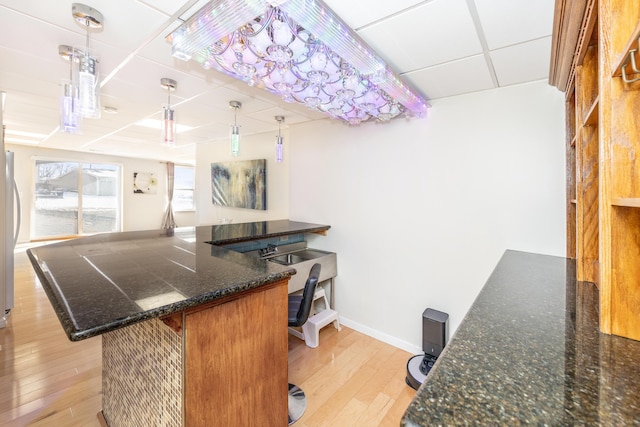 kitchen featuring pendant lighting, light hardwood / wood-style flooring, a paneled ceiling, a kitchen bar, and kitchen peninsula