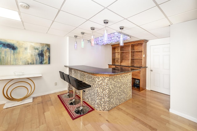 bar with a drop ceiling, hanging light fixtures, and light wood-type flooring