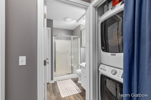 bathroom featuring stacked washer and clothes dryer, toilet, a shower with shower door, track lighting, and hardwood / wood-style flooring