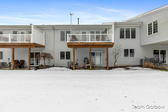 snow covered back of property featuring central AC and a balcony