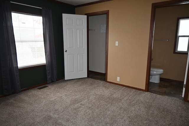 unfurnished bedroom featuring dark carpet and ensuite bath