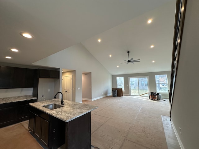 kitchen featuring sink, high vaulted ceiling, ceiling fan, light stone countertops, and a kitchen island with sink