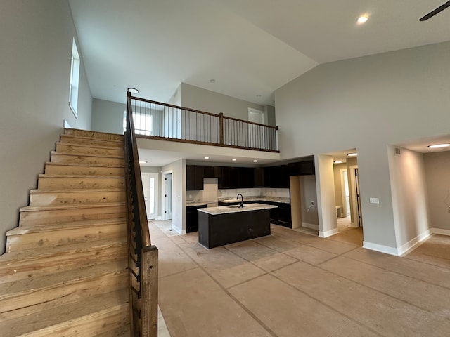 kitchen featuring decorative backsplash, sink, high vaulted ceiling, and a center island with sink