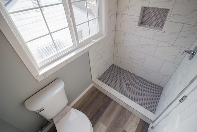 bathroom with wood-type flooring, a tile shower, and toilet