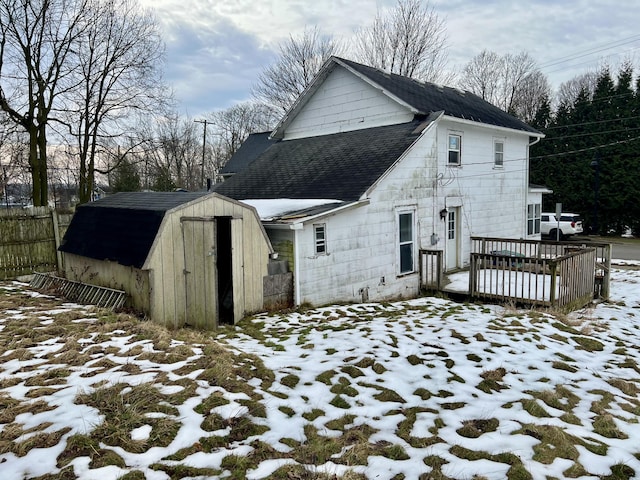 snow covered back of property with a wooden deck and a storage unit