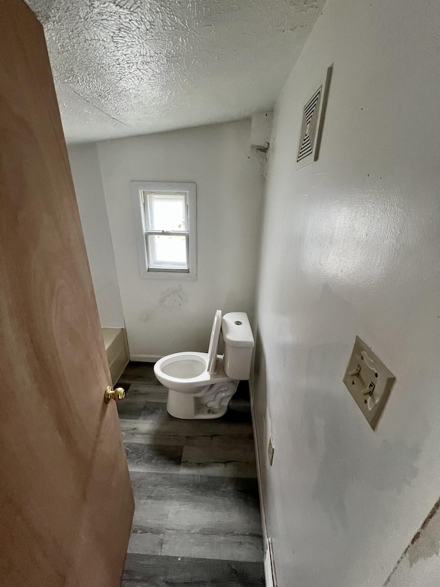 bathroom with wood-type flooring, a bathing tub, a textured ceiling, and toilet