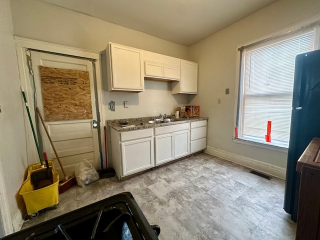 kitchen with dark stone countertops, sink, black refrigerator, and white cabinets