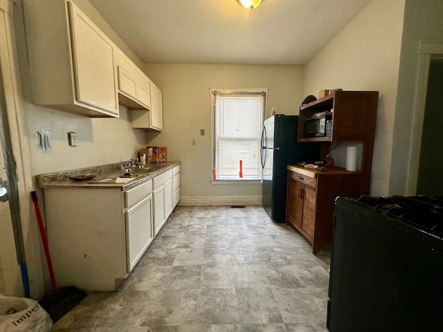 kitchen featuring sink, range with gas cooktop, white cabinets, and black fridge