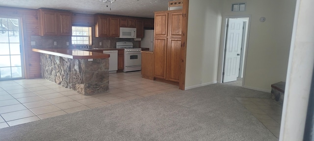 kitchen featuring sink, light colored carpet, a textured ceiling, kitchen peninsula, and white appliances