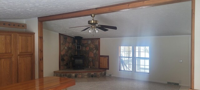 unfurnished living room with ceiling fan, a wood stove, and a textured ceiling