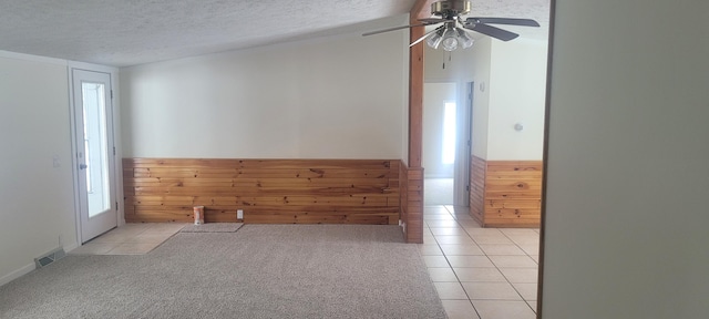 unfurnished room featuring light tile patterned flooring, ceiling fan, wooden walls, and a textured ceiling