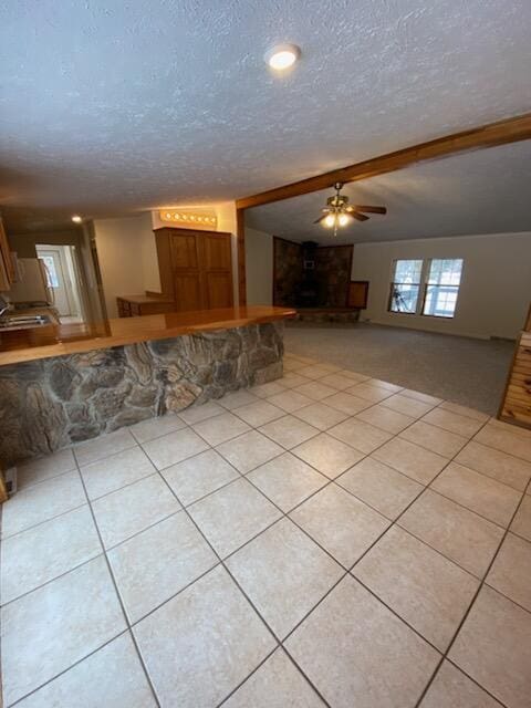 unfurnished living room featuring ceiling fan, beamed ceiling, a textured ceiling, and light tile patterned flooring