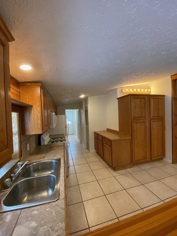 kitchen featuring sink, light tile patterned floors, white appliances, and a textured ceiling