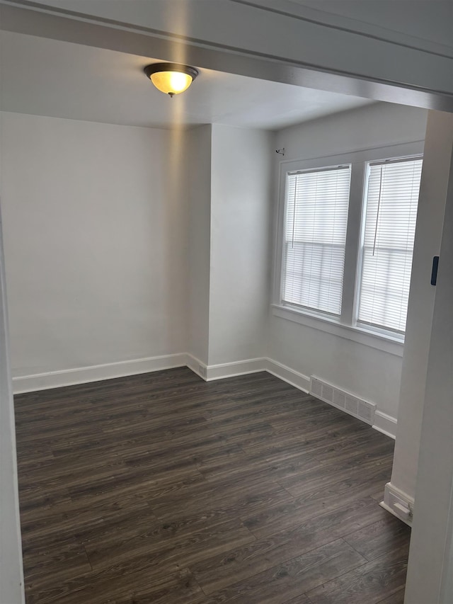unfurnished room with baseboards, dark wood-style flooring, and visible vents