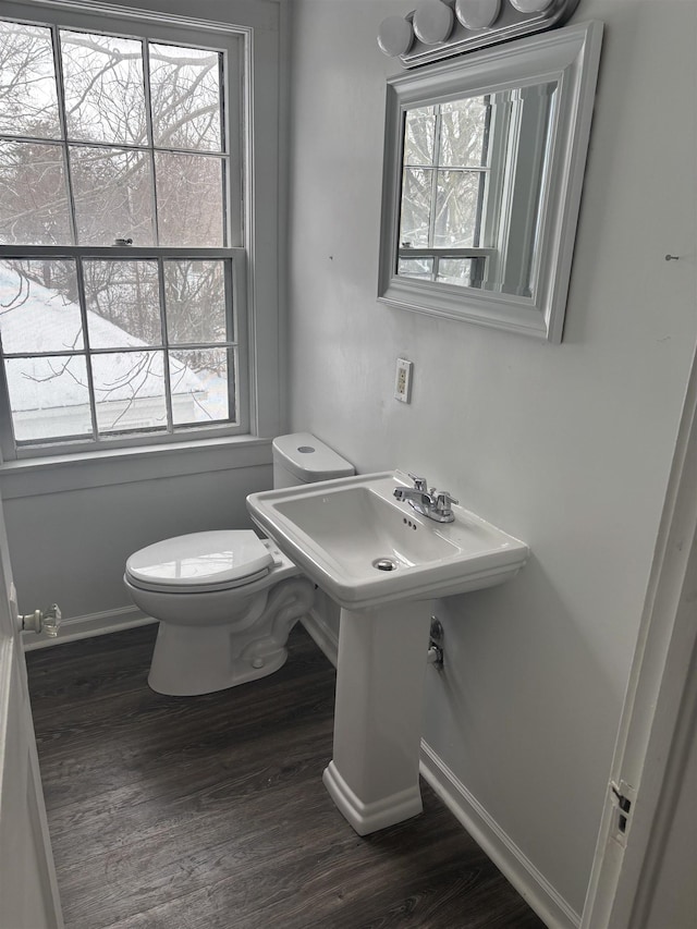 half bathroom with baseboards, toilet, wood finished floors, and a wealth of natural light