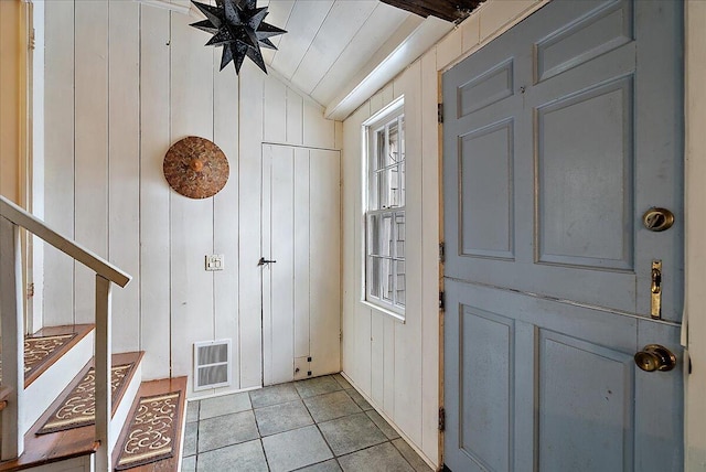 entryway featuring light tile patterned flooring, vaulted ceiling, and wood walls