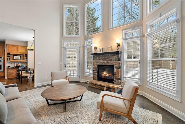 living room with a stone fireplace, dark wood-type flooring, a wealth of natural light, and a towering ceiling