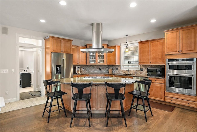 kitchen with a breakfast bar area, hanging light fixtures, a kitchen island, island exhaust hood, and stainless steel appliances