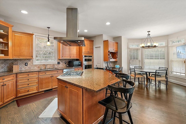 kitchen with pendant lighting, island range hood, light stone counters, and a kitchen island