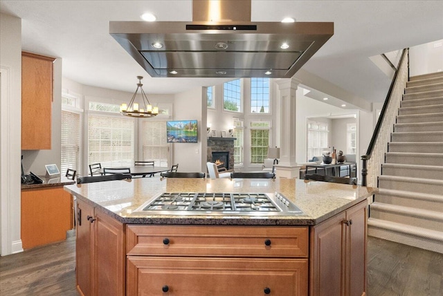 kitchen featuring stainless steel gas cooktop, extractor fan, a center island, pendant lighting, and light stone countertops