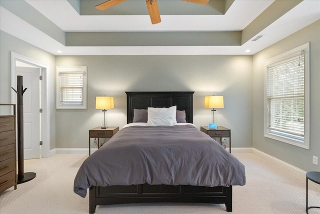 carpeted bedroom with a raised ceiling and ceiling fan