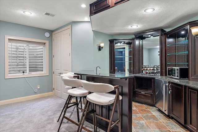 kitchen with a breakfast bar, dark brown cabinets, a textured ceiling, fridge, and carpet