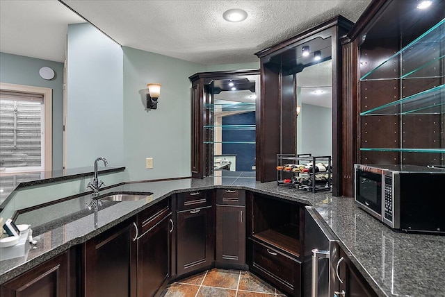 kitchen with sink, a textured ceiling, dark brown cabinetry, and dark stone counters