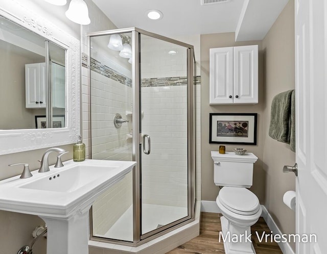 bathroom featuring hardwood / wood-style flooring, a shower with shower door, and toilet