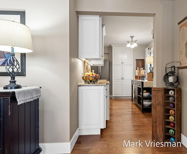 kitchen with white cabinetry, light stone countertops, an inviting chandelier, and light wood-type flooring