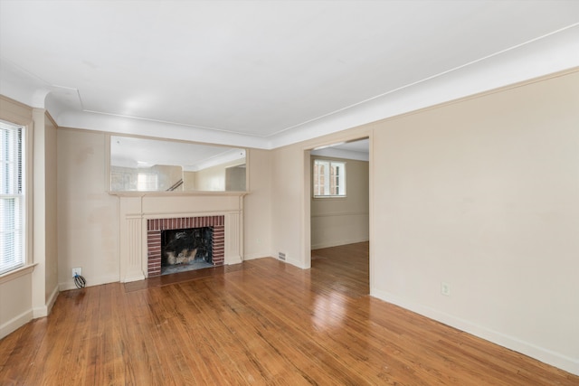 unfurnished living room with wood-type flooring and a brick fireplace