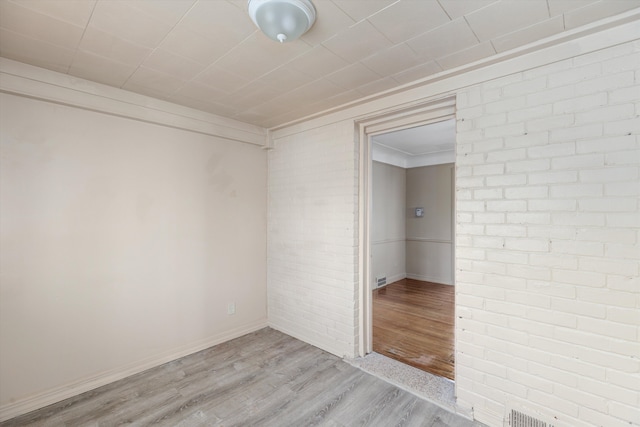 spare room with brick wall and light wood-type flooring