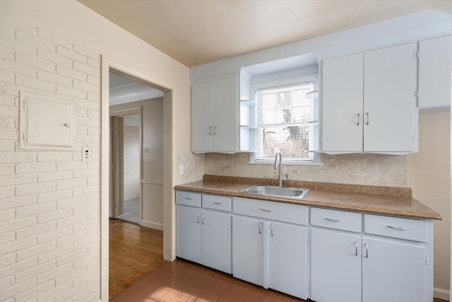 kitchen with white cabinetry, sink, wood-type flooring, and brick wall