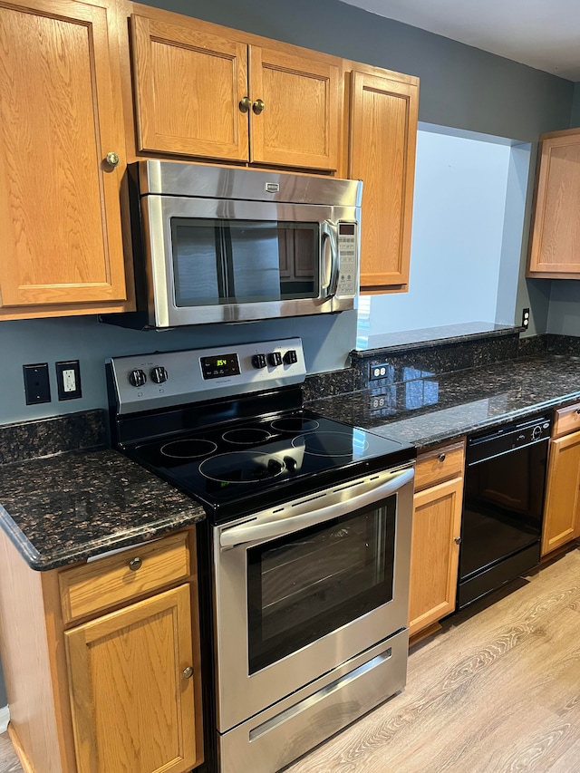 kitchen with dark stone countertops, stainless steel appliances, and light hardwood / wood-style floors