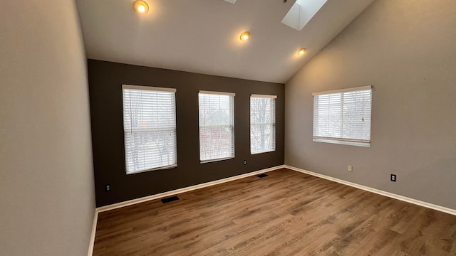 spare room featuring high vaulted ceiling, a skylight, and hardwood / wood-style floors