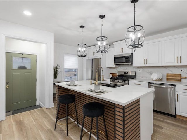 kitchen with white cabinetry, decorative light fixtures, a center island with sink, appliances with stainless steel finishes, and light hardwood / wood-style floors