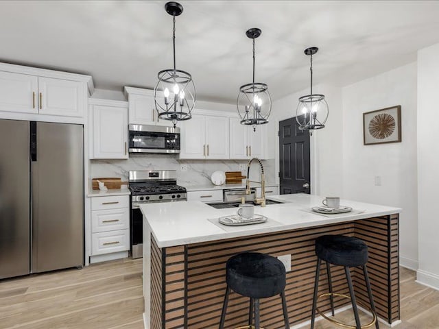 kitchen featuring appliances with stainless steel finishes, pendant lighting, white cabinetry, sink, and a center island with sink