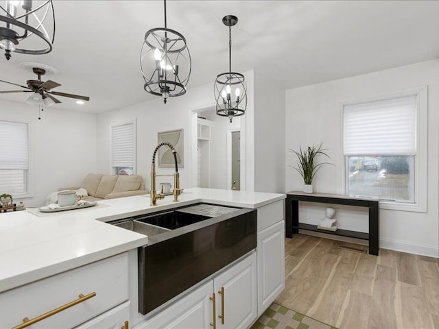 kitchen featuring sink, white cabinetry, decorative light fixtures, light hardwood / wood-style floors, and ceiling fan with notable chandelier