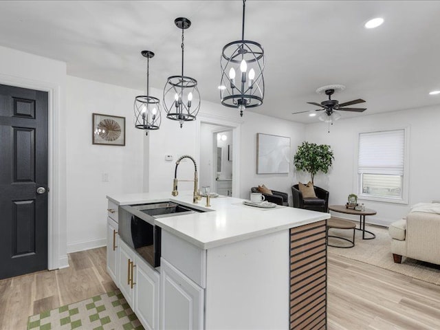 kitchen with sink, light hardwood / wood-style floors, an island with sink, white cabinets, and decorative light fixtures