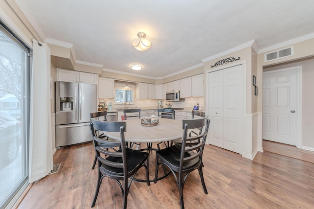 dining area with ornamental molding, sink, and light wood-type flooring