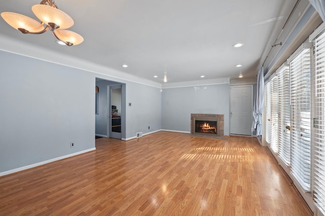 unfurnished living room with a warm lit fireplace, recessed lighting, visible vents, baseboards, and light wood-type flooring