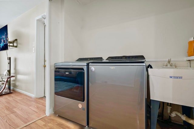 washroom featuring washing machine and clothes dryer, light wood-style floors, a sink, laundry area, and baseboards