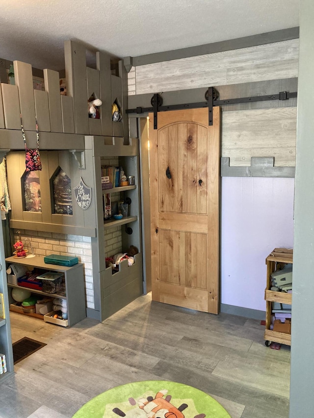 game room featuring wood-type flooring, a barn door, and a textured ceiling