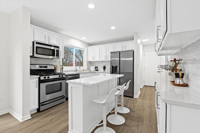 kitchen featuring stainless steel appliances, a kitchen island, white cabinets, and light hardwood / wood-style flooring