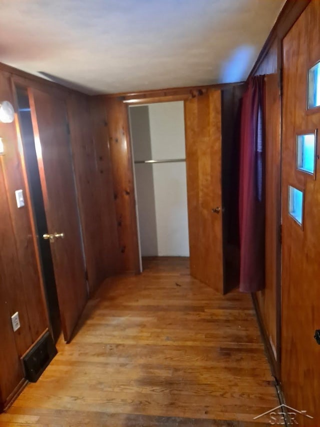 hallway featuring visible vents, wood walls, and light wood finished floors