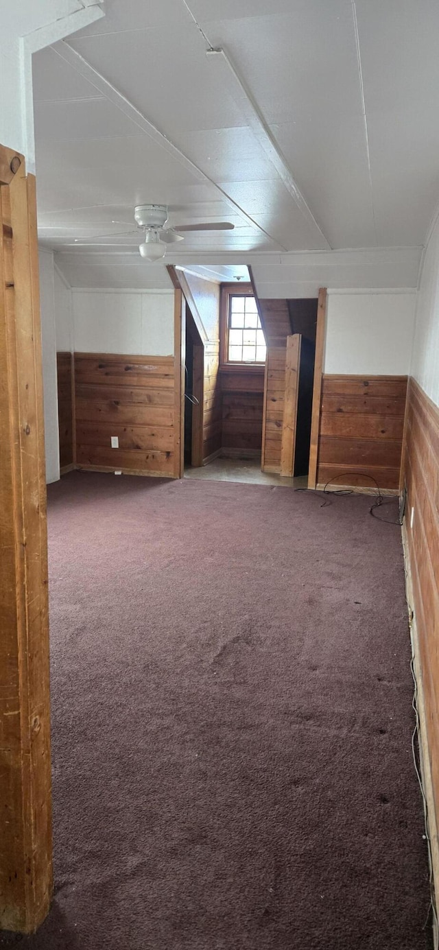 bonus room featuring dark colored carpet and wood walls